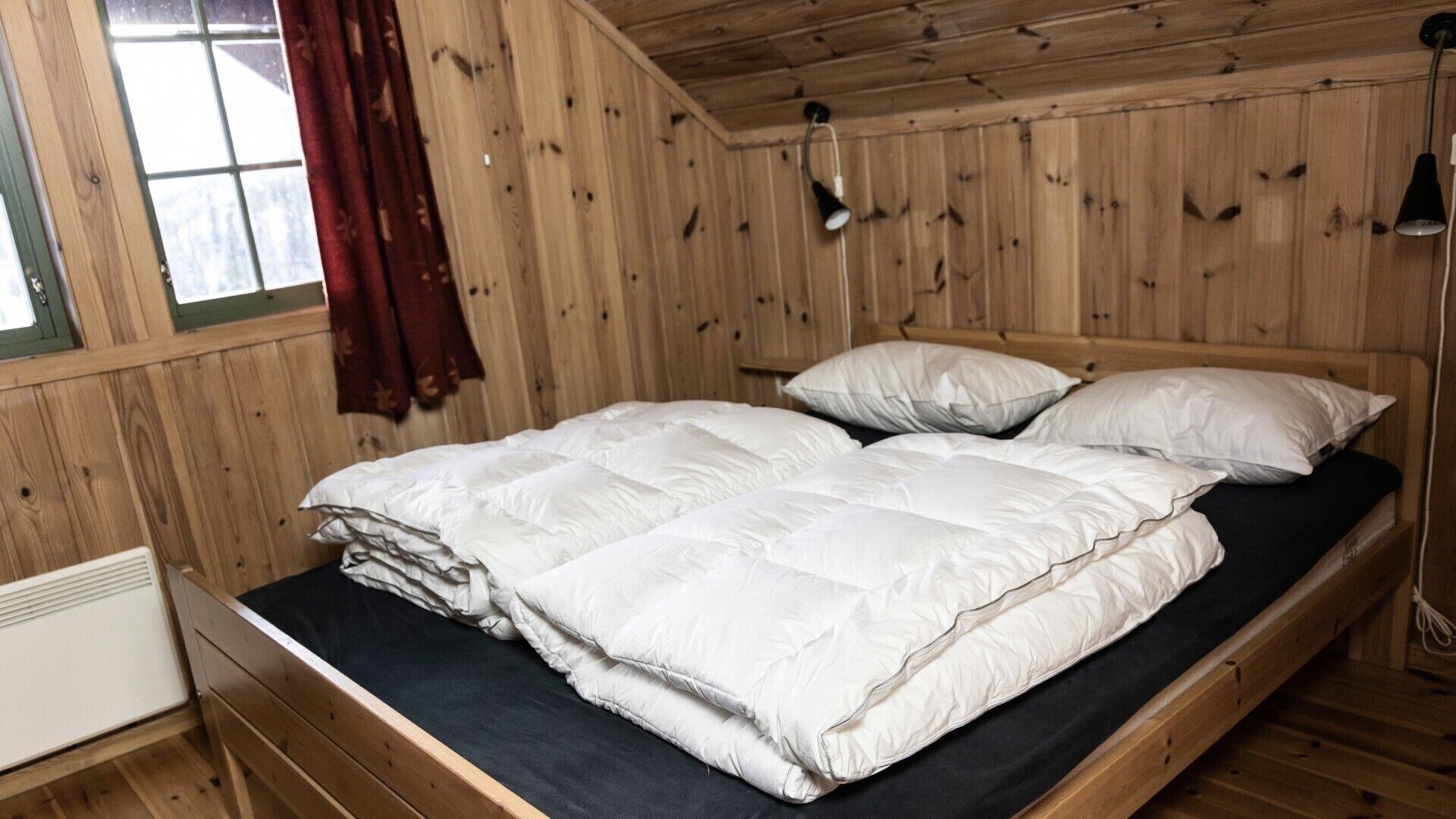 A wooden room with a bed, a window with curtains, and a radiator.
