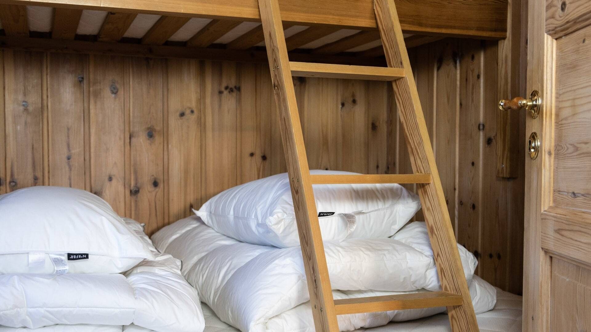A bunk bed with a wooden ladder, white bedding, and a wooden door with a brass handle.