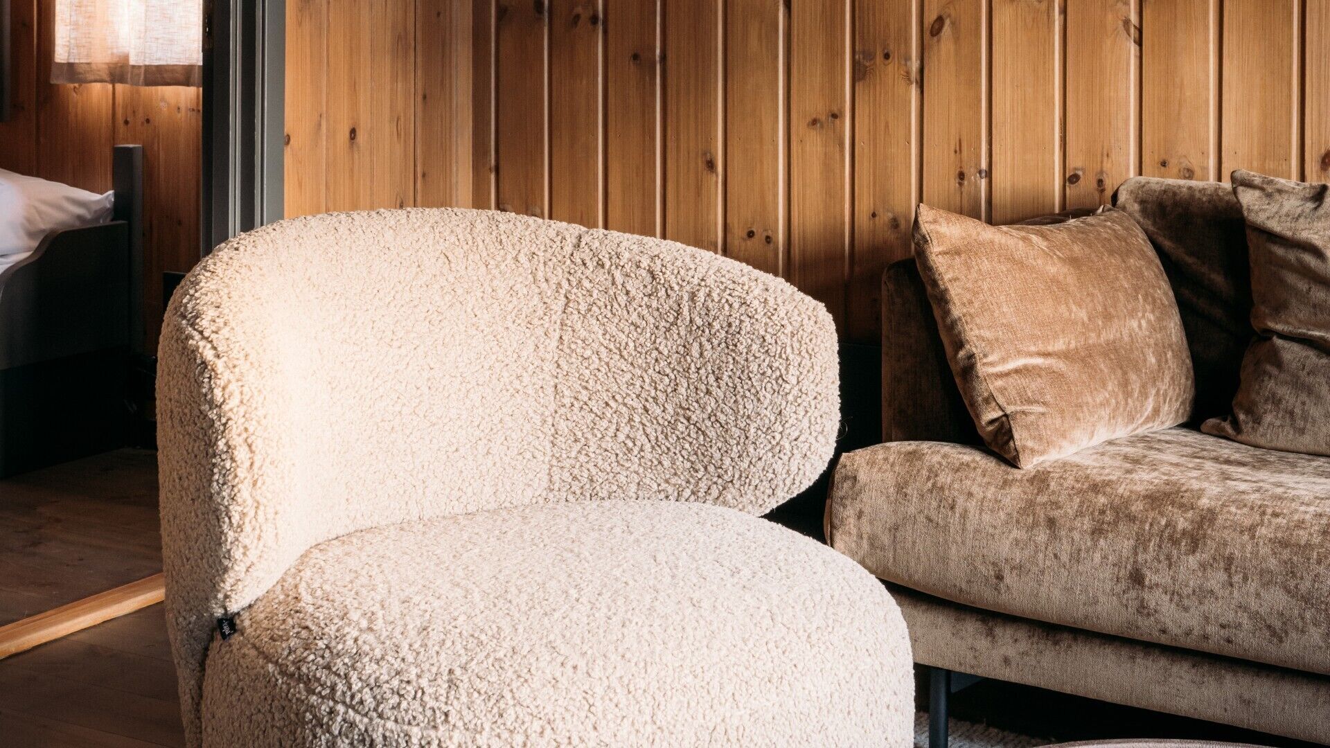 Une pièce avec un mur en bois, un fauteuil beige et un canapé marron avec des coussins.