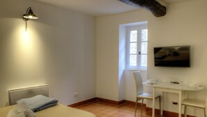 A bedroom with a bed, a bedside table, a chair, a desk, a television, and a window.