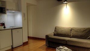 A compact kitchen with a built-in oven and a small refrigerator. A sofa and a coffee table are placed in the living area.