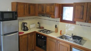 Een compacte keuken met houten kastjes, een magnetron, een koelkast, een fornuis en een spoelbak.