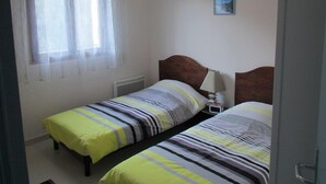 Een kamer met twee eenpersoonsbedden, een raam met dunne gordijnen, een klein nachtkastje met een lamp en een lijst met een afbeelding aan de muur.