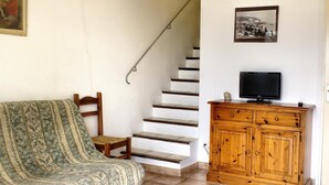 A staircase with a handrail, a wooden cabinet with a television, and a patterned sofa. - Espace des Oliviers - Gîte n°2 (CASTAGNIERS)