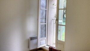 A corner of a room with a white wall, a window with white shutters, and a vent on the wall. - Espace des Oliviers - Gîte n°2 (CASTAGNIERS)