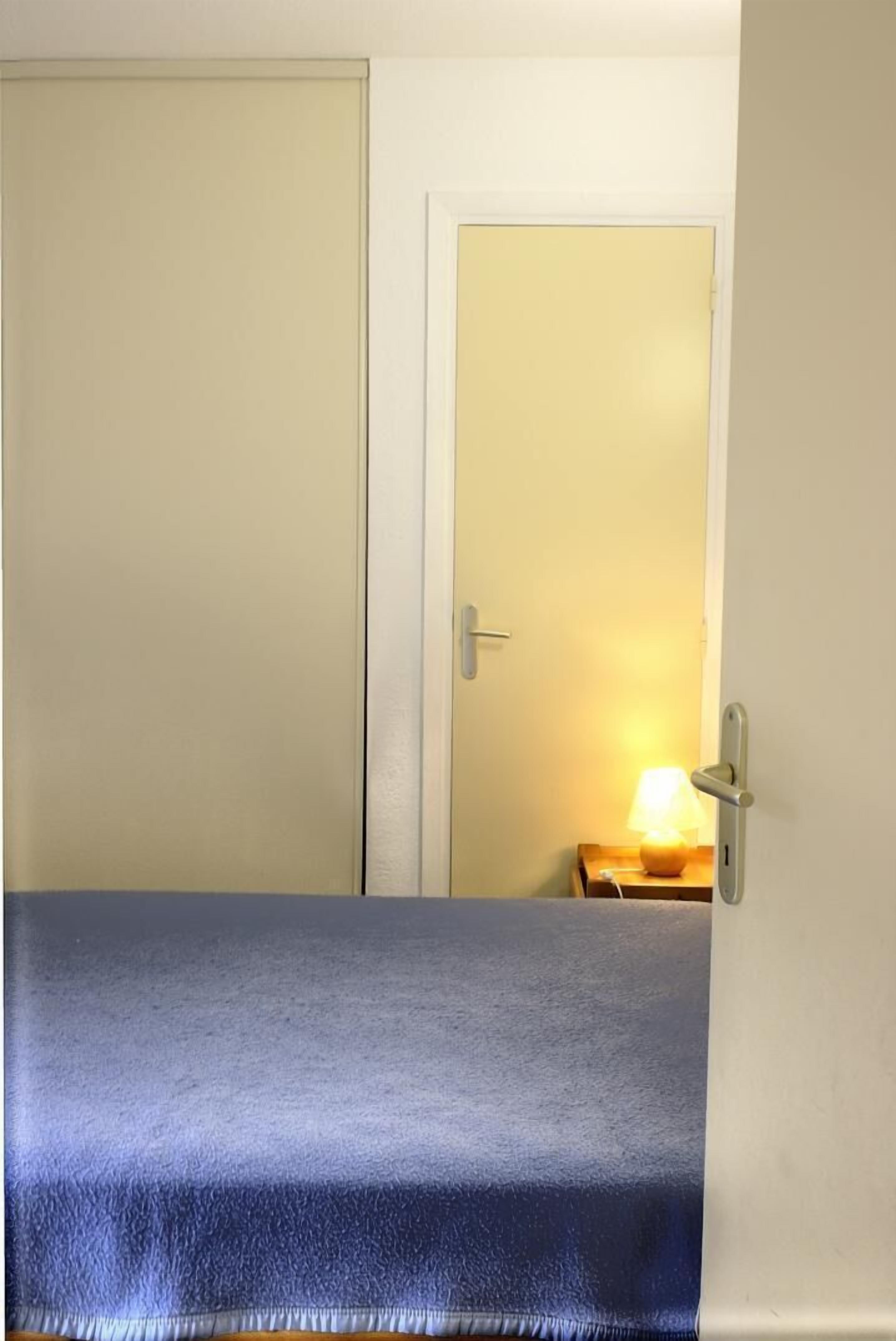 A room with a bed, a door, and a nightstand with a lamp.