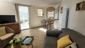 A living room with a TV, wicker sofa, and a dining area with a table and chairs.