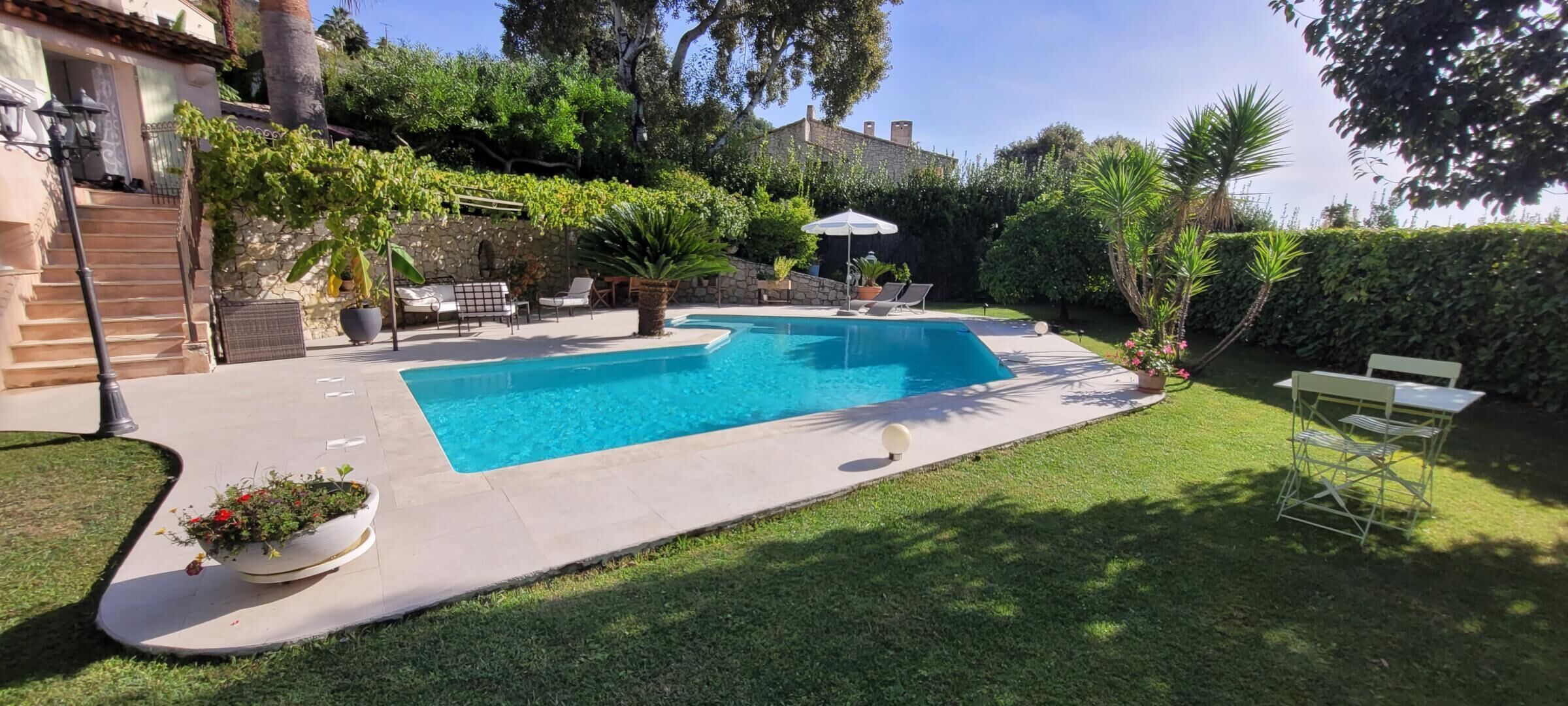 A rectangular swimming pool with a stone border, surrounded by a grassy lawn and potted plants.