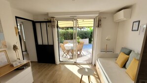 A compact living space with a sliding glass door leading to an outdoor patio, a sofa with cushions, a small round table, and a white cabinet.