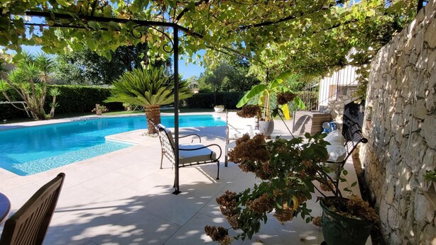 A swimming pool with a pergola, chairs, and potted plants.