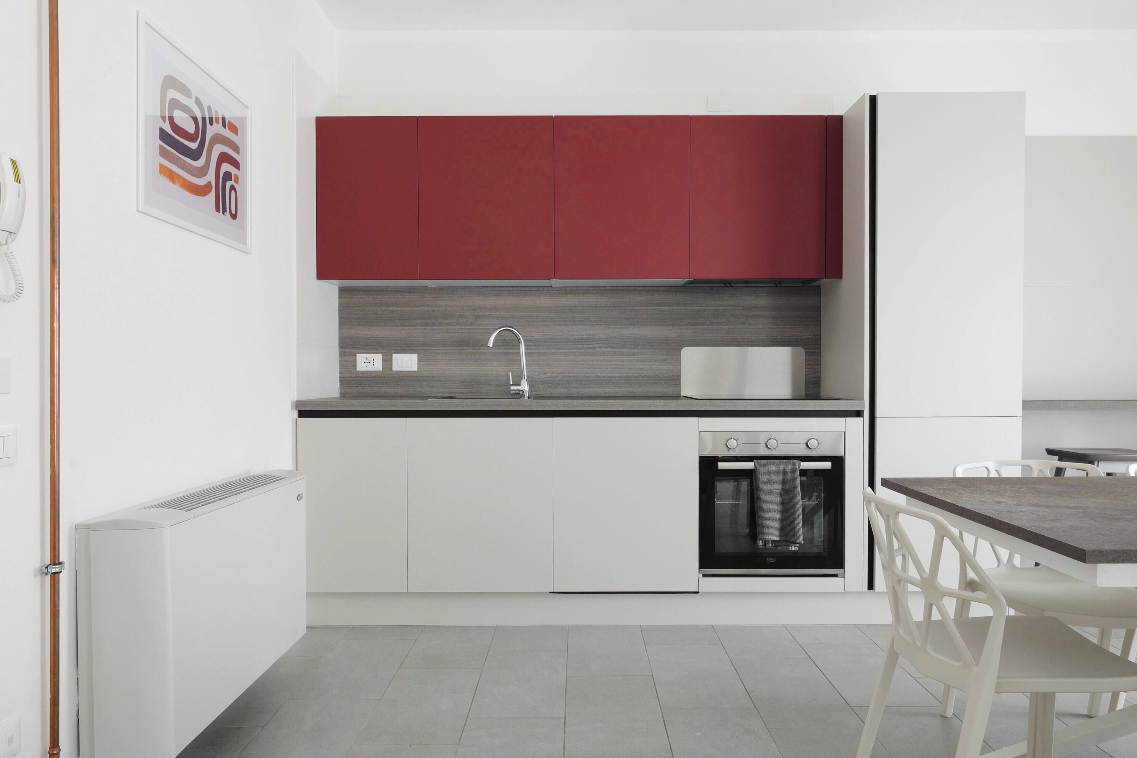 Une cuisine moderne avec des meubles blancs, un meuble supérieur rouge, un évier en acier inoxydable et un four encastré.