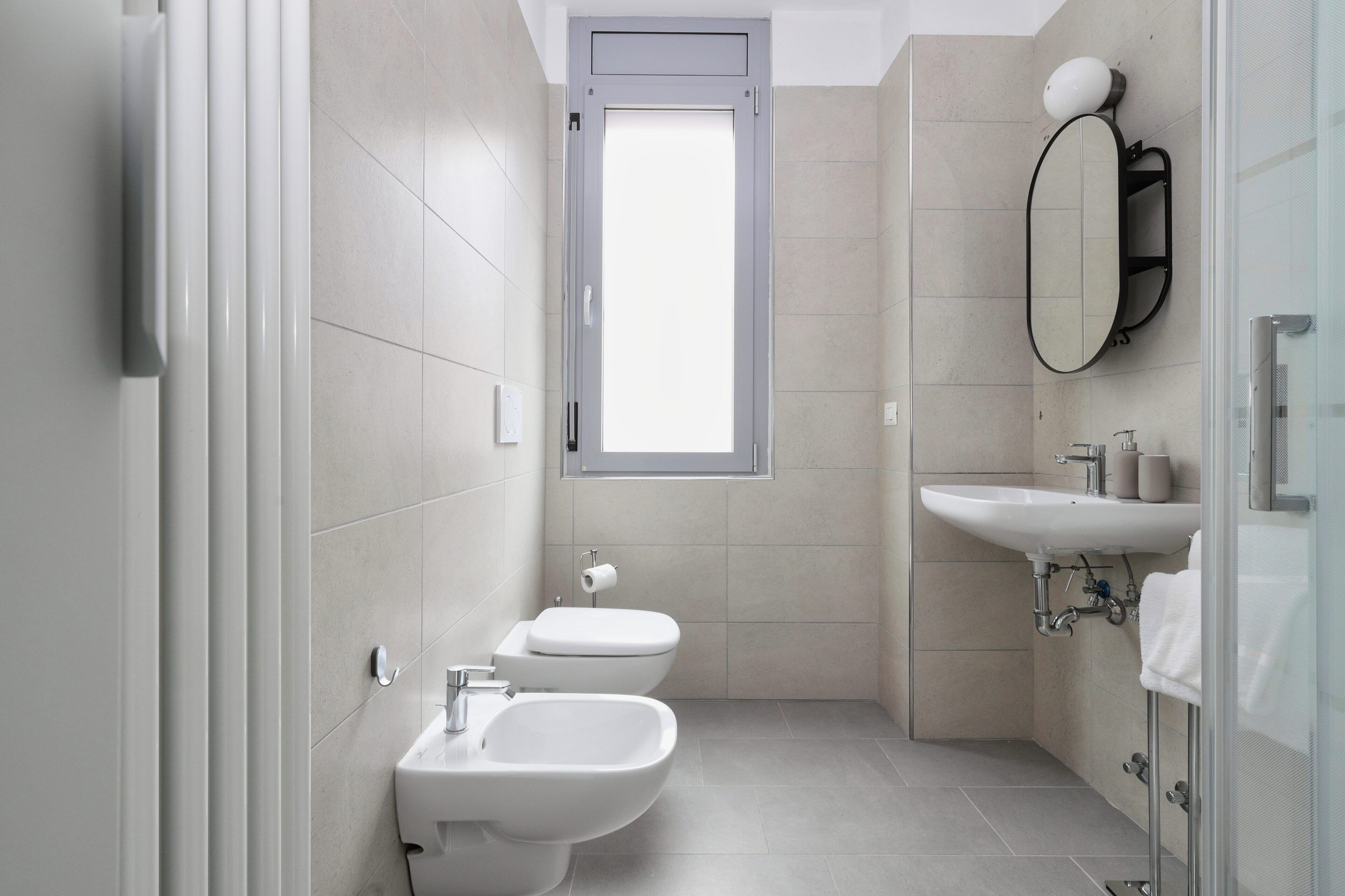 A modern bathroom with two toilets, a bidet, a sink, and a mirror.