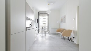 Una cocina moderna con armarios blancos, una zona de comedor con dos sillas y vistas al exterior a través de un ventanal.