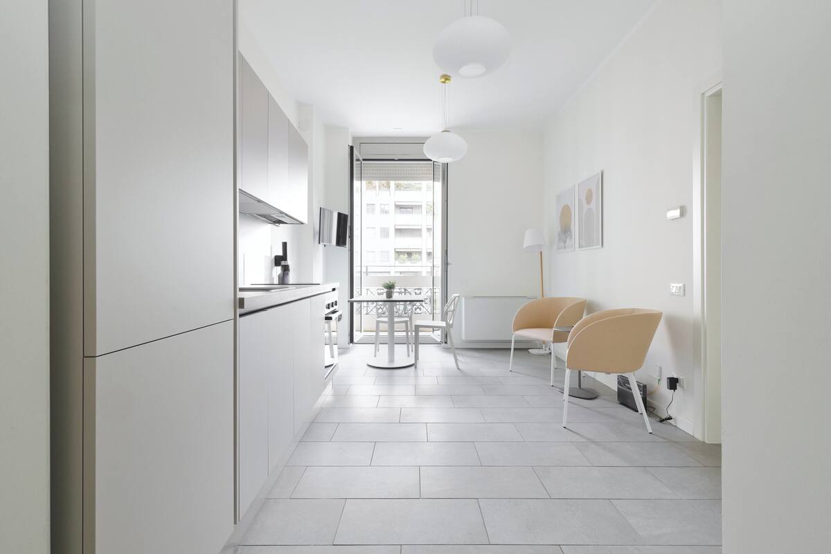 A modern kitchen with white cabinets, a dining area with two chairs, and a view of the outside through a glass door.