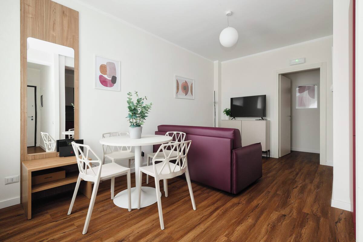 A modern living room with a wooden floor, white furniture, a purple sofa, and a flat-screen TV.