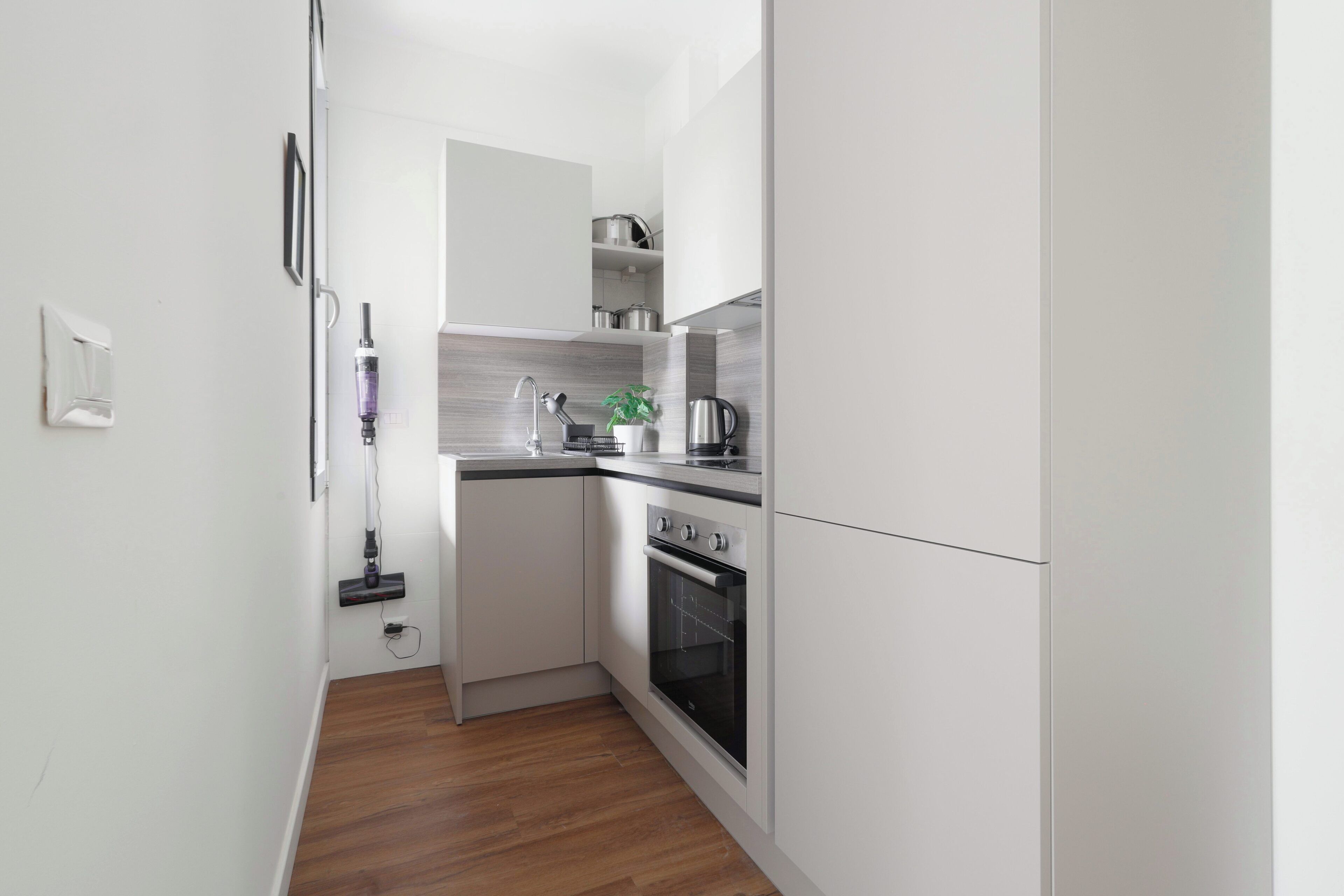 A narrow kitchen with white cabinets, a built-in oven, and a coffee maker.