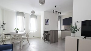 Una cocina moderna con zona de comedor, muebles blancos y un televisor de pantalla plana.