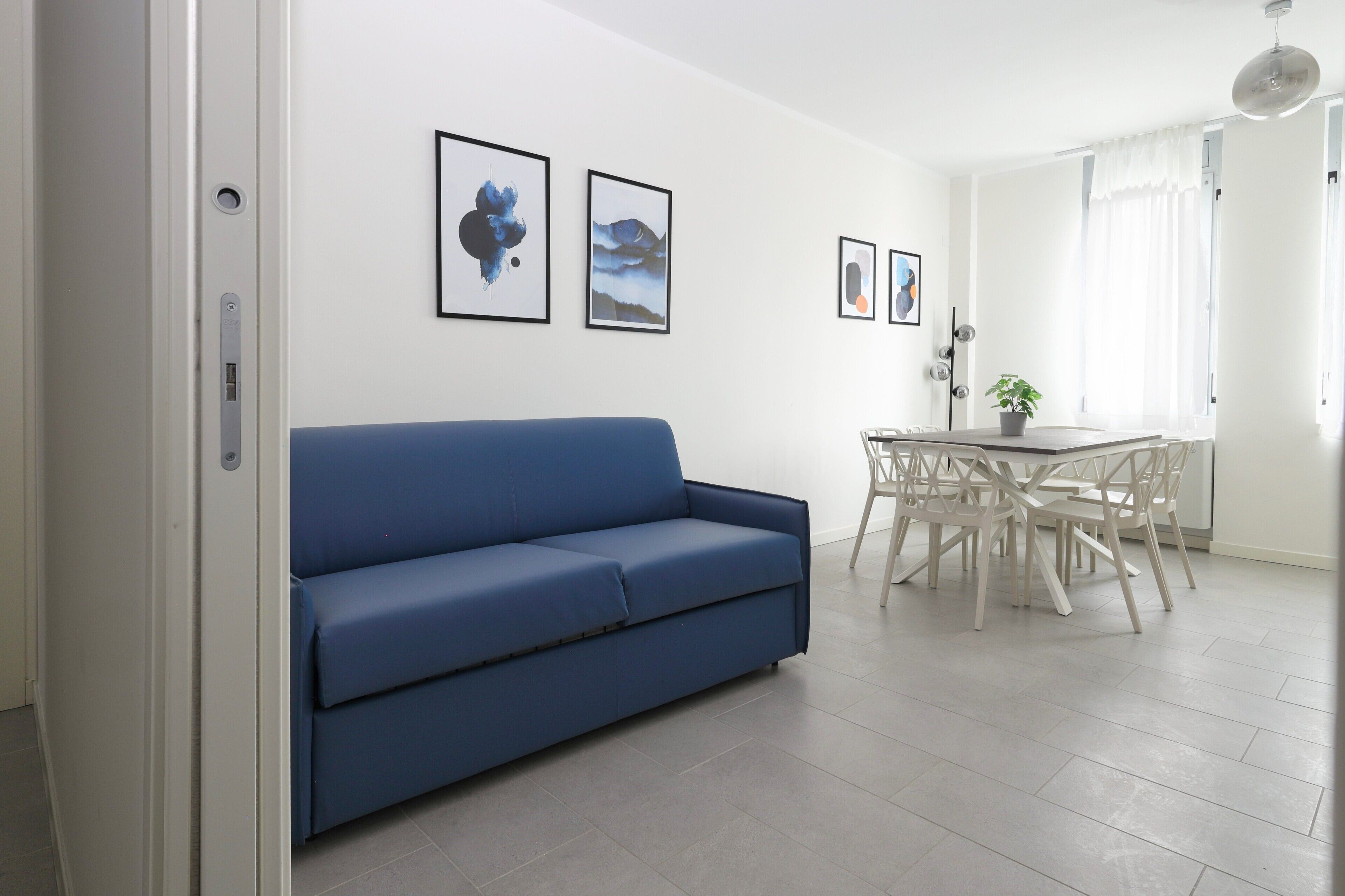 Una sala de estar moderna con un sofá azul, una mesa de comedor con sillas y obras de arte enmarcadas en la pared.