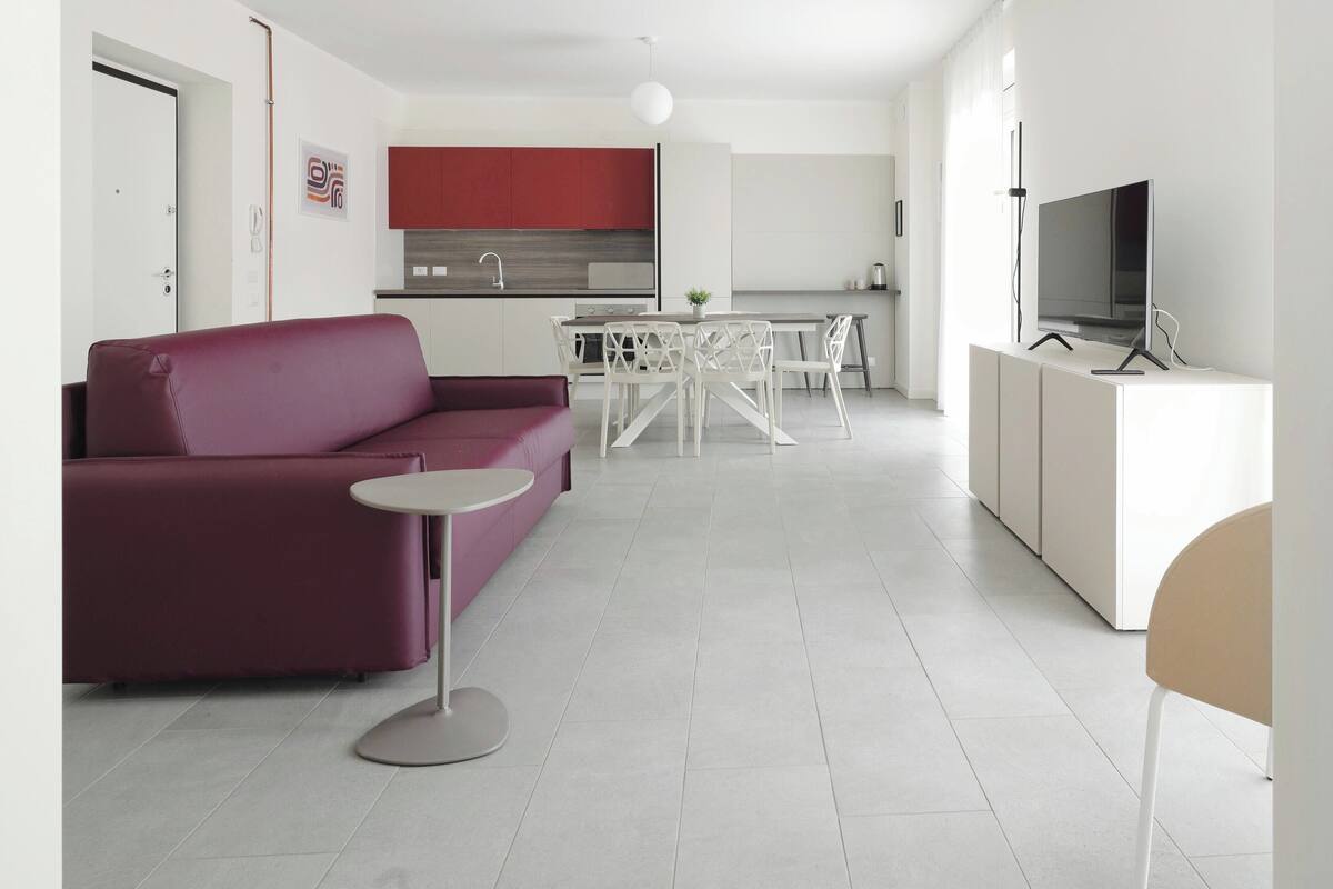 A modern living room with a red sofa, a small round table, and a TV on a stand.