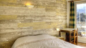 A bedroom with a wooden wall, a bed, a desk with a chair, and a window with curtains. - Le Baousset - SIGALE (SIGALE)