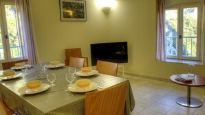 A dining area with a table set for four, chairs, a television, and a window with curtains.