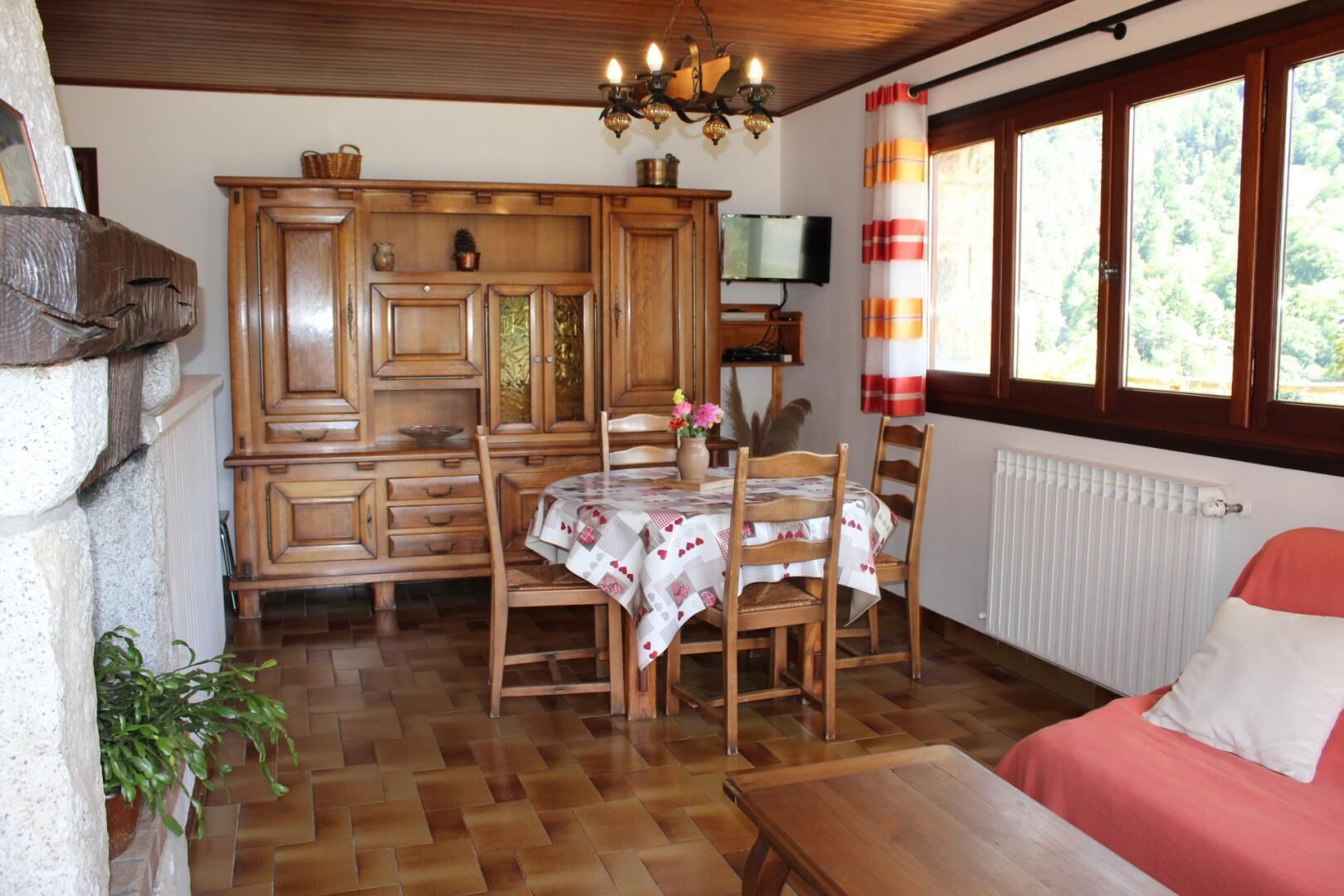 Une pièce chaleureuse avec une table à manger en bois, des chaises, un canapé rouge, une cheminée, un téléviseur et une fenêtre avec des rideaux.
