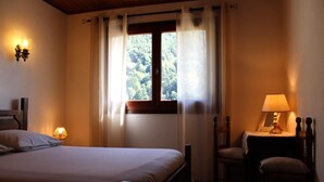 Un dormitorio con cama, una silla, una mesa con lámpara y una ventana con cortinas.