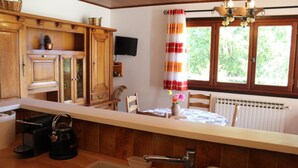 Una cocina con armarios de madera, una cafetera, un lavabo y un ventanal con cortinas.