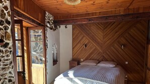Une chambre avec un mur en pierre, un plafond en bois et un lit recouvert d’une couverture blanche et bleue.