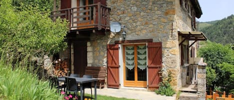 A stone house with a balcony, a wooden door, and a small garden with flowers.