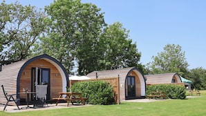 A row of wooden cabins with arched doorways, each with a small patio and a picnic table. - Honeypot Hideaways - Manuka (Chester)