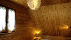 Een houten kamer met een bed, een raam met gordijnen, een lamp en een radiator.