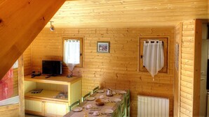 Een knus houten vakantiehuisje met een eethoek, een televisie en een kleine keuken.