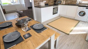 Eine moderne Küche mit weißen Schränken, einem Holztisch gedeckt mit Tellern und Gläsern sowie einer Waschmaschine in der Ecke.