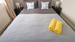 Ein ordentlich bezogenes Bett mit einem gemusterten Überwurf, zwei Kissen und einem aufgerollten gelben Handtuch.