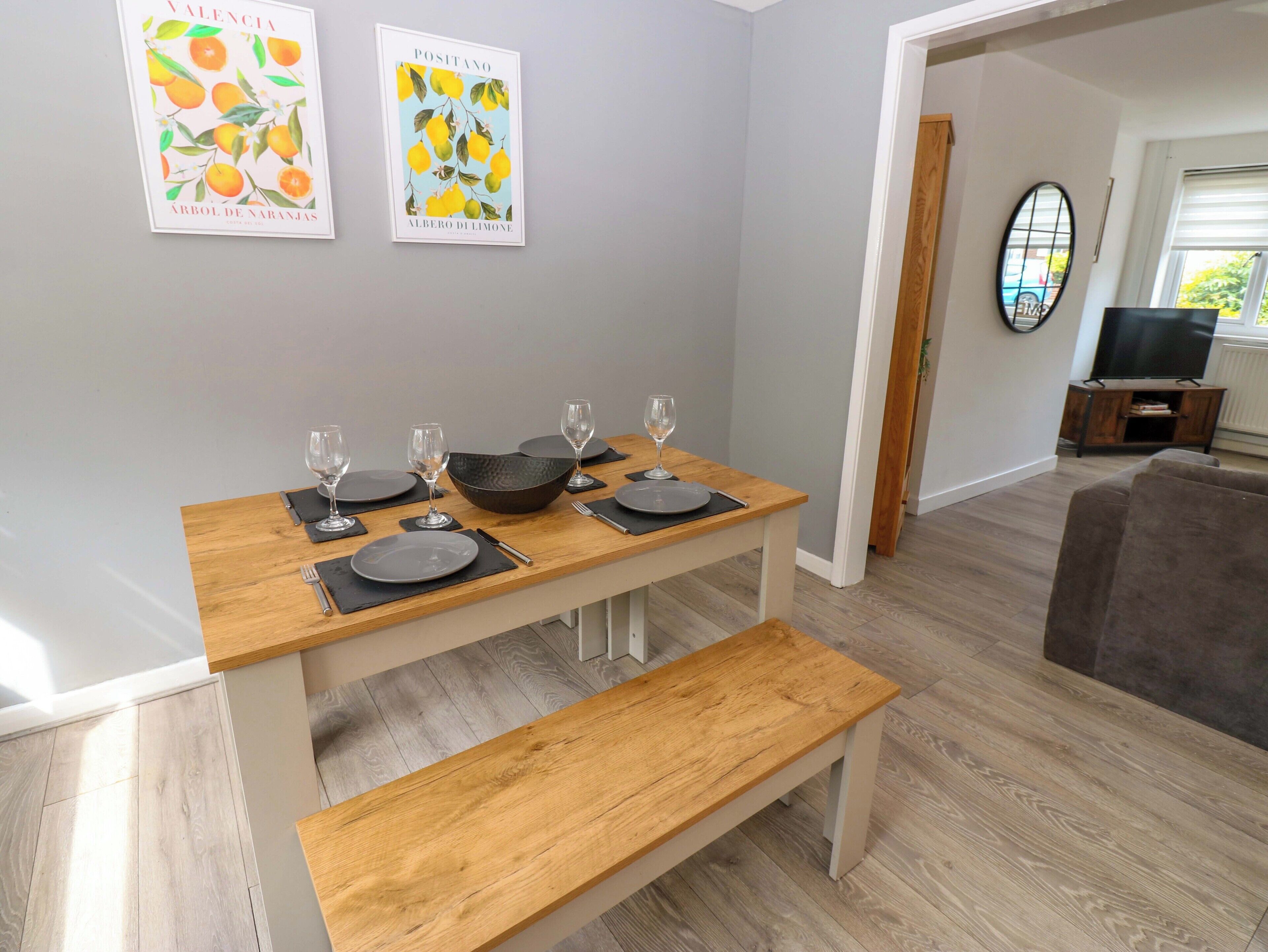 A dining area with a wooden table set for four, a bench, and two framed pictures on the wall.