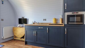 Una cocina compacta con cubierta de madera, armarios oscuros, un microondas integrado y un lavamanos pequeño.