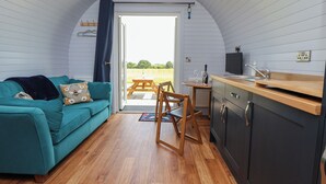 Un interior acogedor con un sofá azul turquesa, una mesa de comedor de madera y una zona de cocina con un lavabo y armarios.