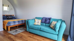 Una habitación acogedora con una cama de madera, un sofá color turquesa y piso de madera.