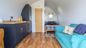 Una habitación compacta con kitchenette, una cama con manta escocesa y un sofá color turquesa.