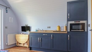 A kitchen with a wooden table, a microwave, and cabinets. - Honeypot Hideaways - Clover (Chester)