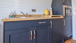 A modern kitchen with a wooden countertop, a sink, and dark cabinets with metallic handles. - Honeypot Hideaways - Clover (Chester)