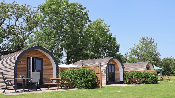 A row of wooden cabins with arched doorways, each with a small patio and a picnic table. - Honeypot Hideaways - Clover (Chester)