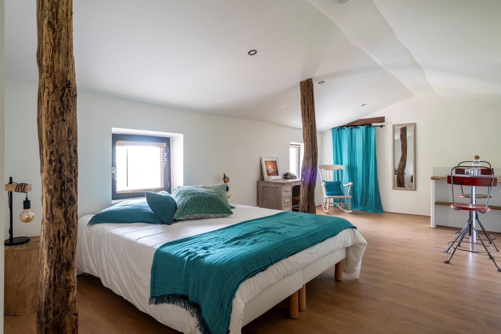 A bedroom with a large bed, a desk, a chair, and a mirror.
