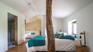 A bedroom with a large bed, a wooden tree trunk, a small wooden stool, and a window with blinds.