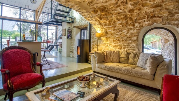 A cozy living room with a stone wall, a red armchair, a beige sofa, and a glass coffee table with magazines.