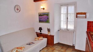 A cozy room with a sofa, a wall clock, a painting, a lamp, and a window with a view of the outdoors. - Les Mesanges aux Baux (SERANON)