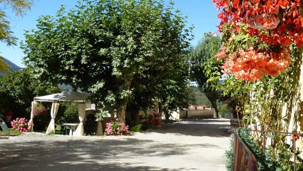 A garden area with a pergola, a large tree, and a wall covered in red flowers. - Les Mesanges aux Baux (SERANON)