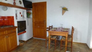 A compact kitchen with a tiled backsplash, wooden cabinets, a stove, and a dining table set for four. - Les Mesanges aux Baux (SERANON)