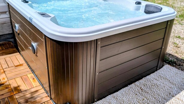 A hot tub with a wooden exterior, a control panel, and a wooden deck.